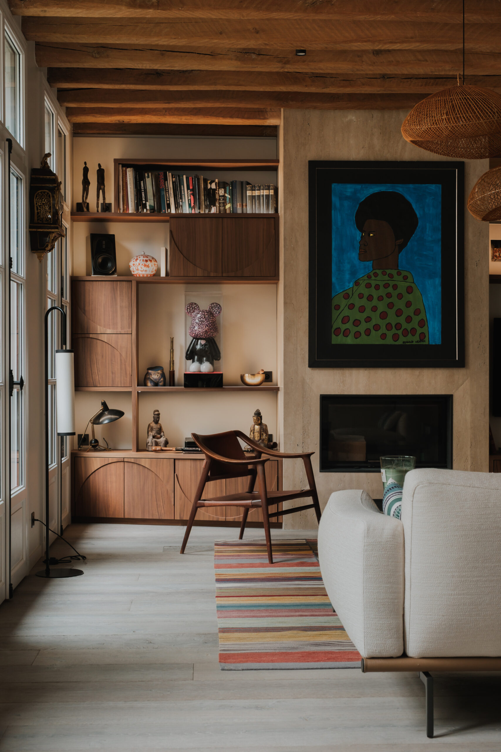 Aménagement de salon sur mesure, bibliothèque en noyer avec façades aux motifs géométriques, rangements intégrés, espace bureau, cheminée contemporaine, poutres apparentes, matériaux nobles, design élégant et ambiance chaleureuse.