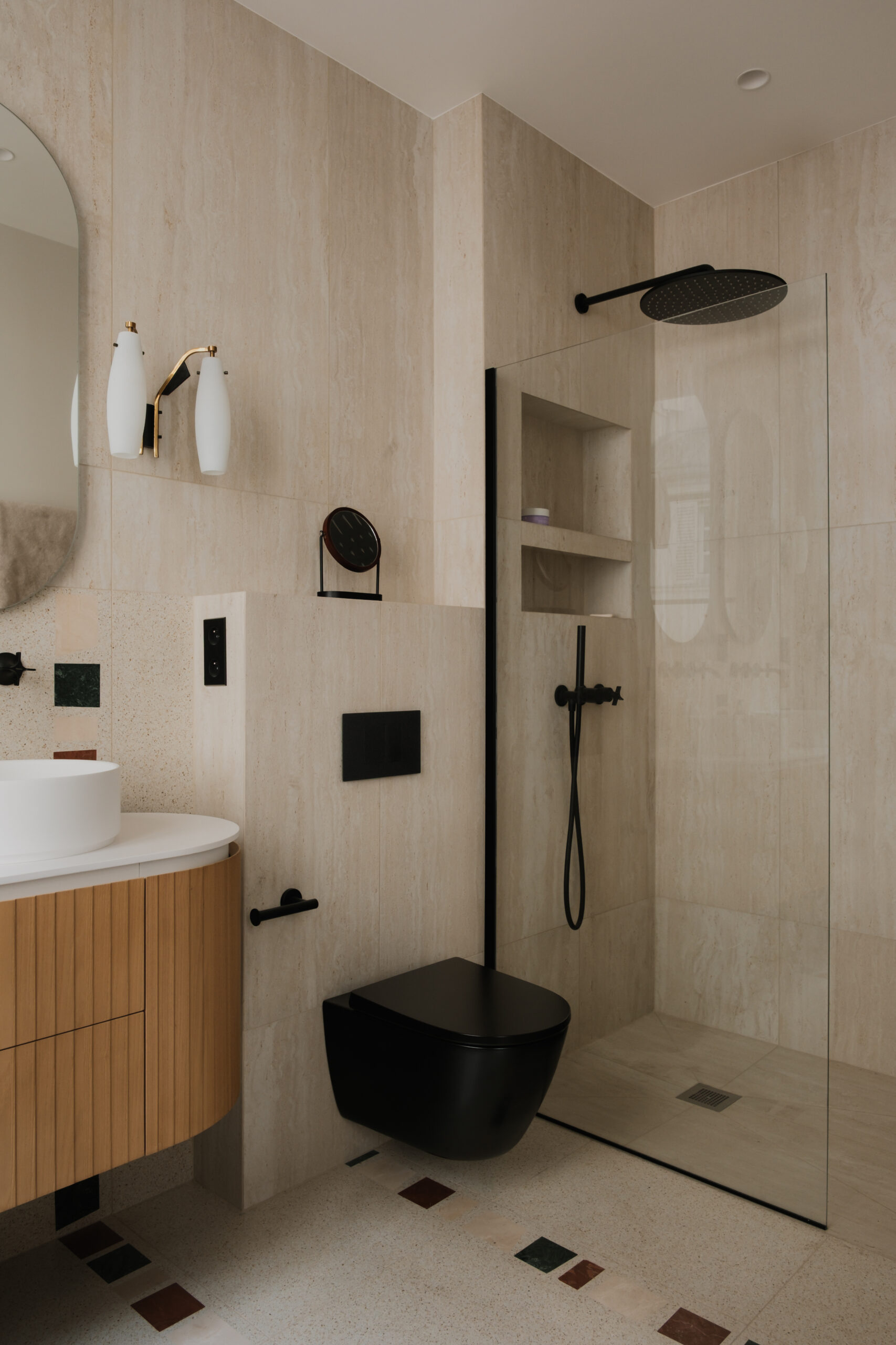 Salle de bain sur mesure, meuble vasque en bois, douche à l’italienne en travertin, paroi vitrée, robinetterie noire, niches intégrées, sol en pierre naturelle.