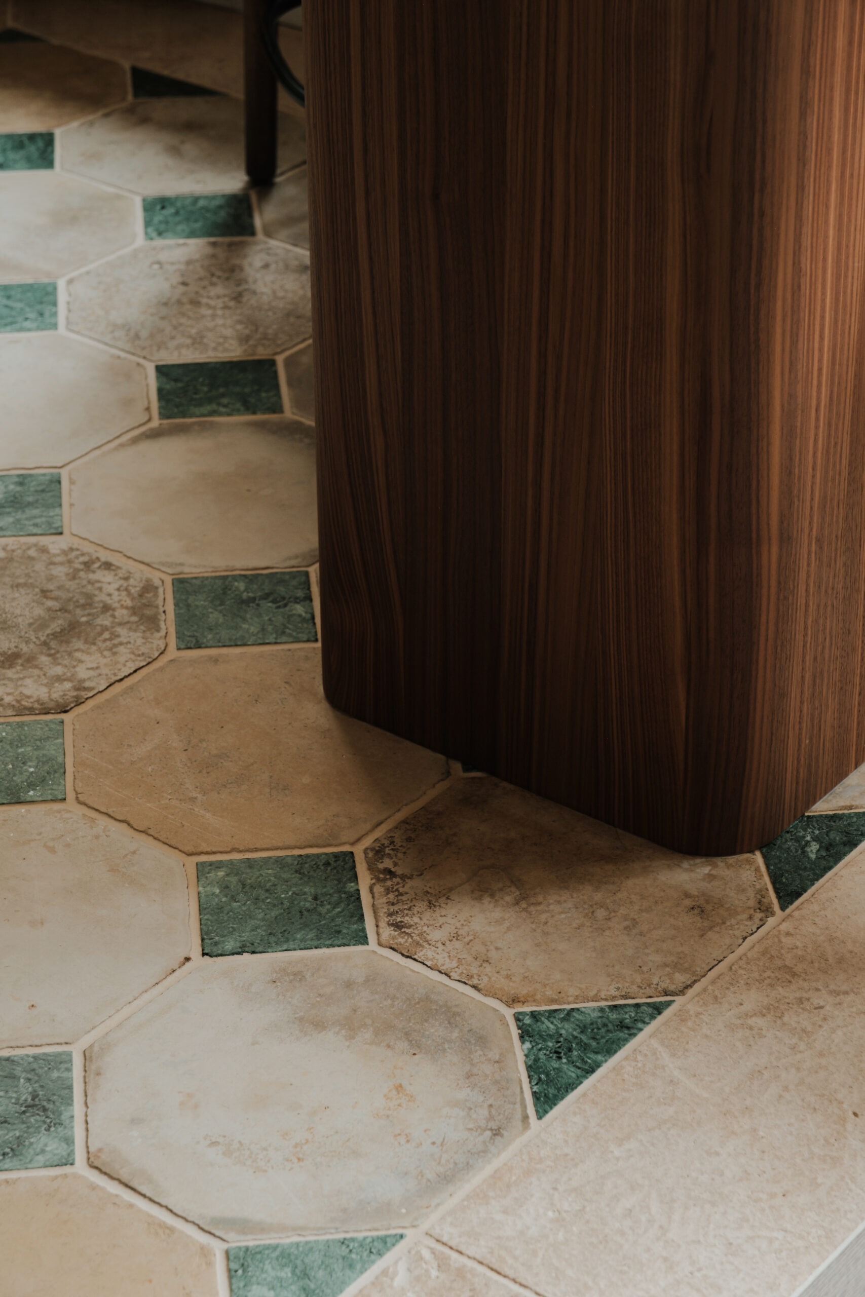 Détail d’aménagement sur mesure, îlot de cuisine en noyer aux lignes arrondies, sol d’époque en pierre de Bourgogne et marbre vert, appartement Saint Germain.
